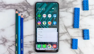 Smartphone displaying various apps on a marble surface with colored pencils and building blocks nearby.