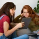Two young girls sitting on a couch, one holding a tablet while the other looks on attentively.