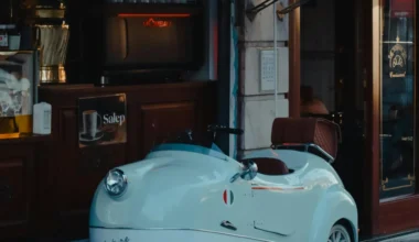 A vintage white microcar with a red interior parked outside a café.